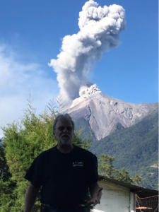 Joseph Behm with a volcano erupting ash in the background